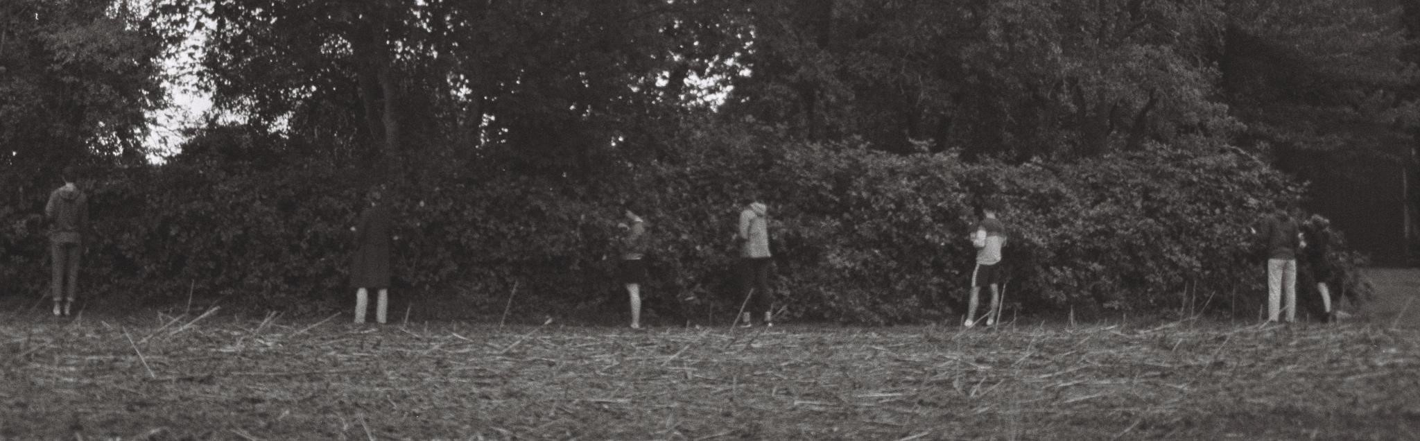 people standing in front of bushes b/w